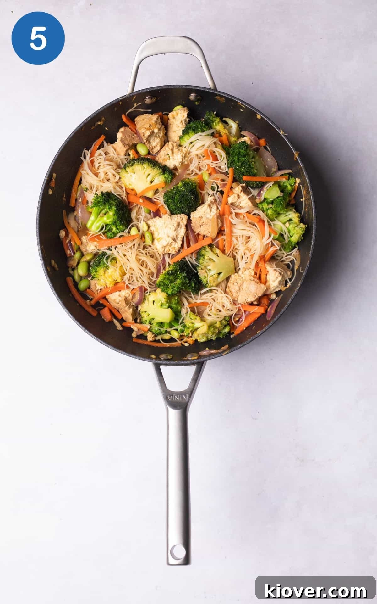 adding noodles and lime juice to the wok pan with vegetables.