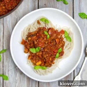 Spaghetti Bolognese topped with fresh basil in a bowl. Bowl is on a wooden background.