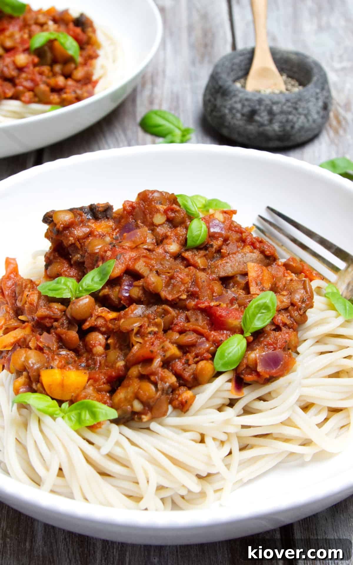 Close up image of spaghetti 20 minute lentil bolognese topped with fresh basil swerved in a white bowl with silver fork. 