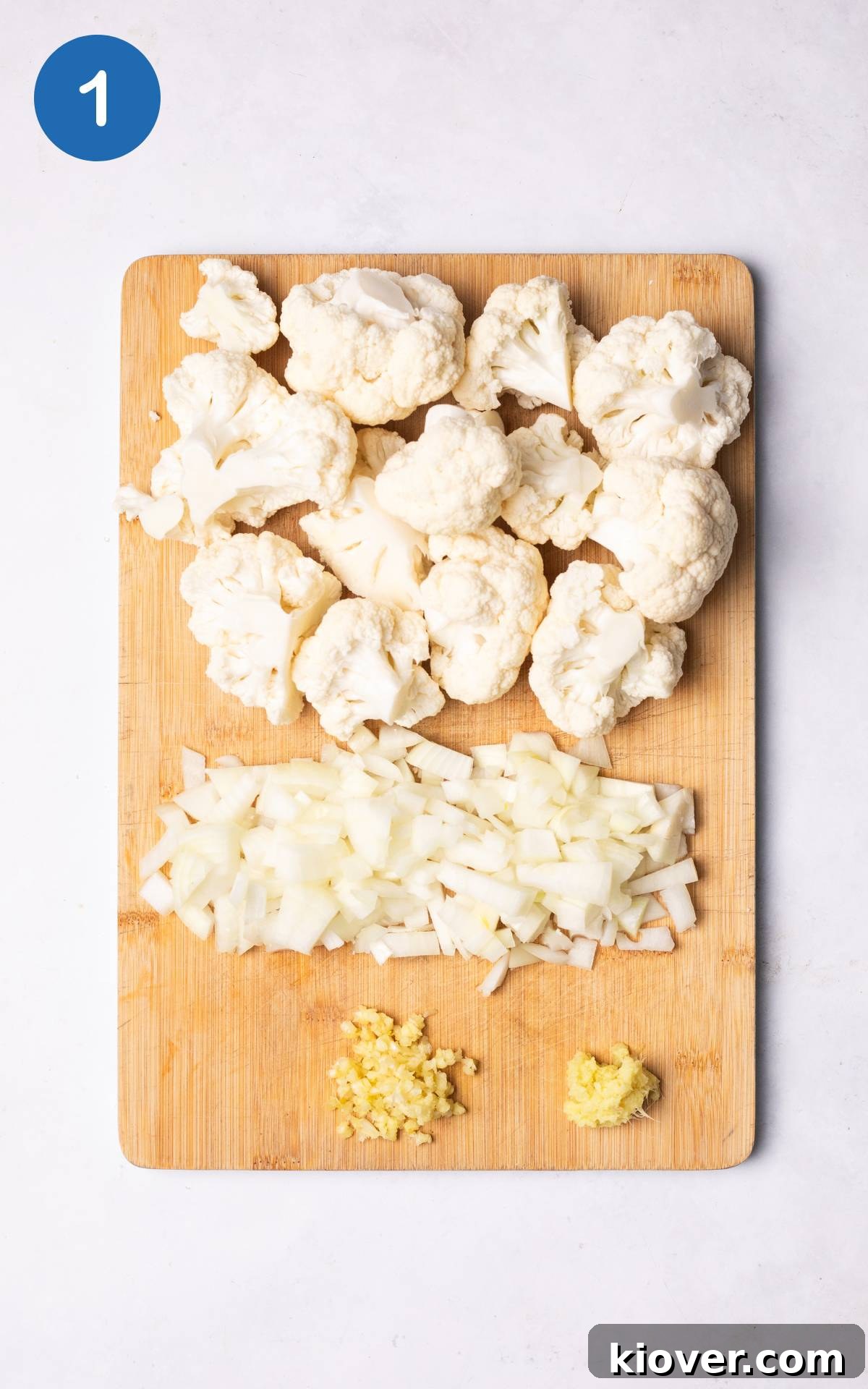 Creamy Roasted Cauliflower Soup Recipe for Cozy Nights 4 onion, ginger, cauliflower and garlic on a wooden cutting board.