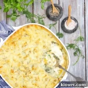 Fish pie being served with silver spoon on a wooden table. There is parsley to accessorise the table, along with small pots of of salt and pepper.