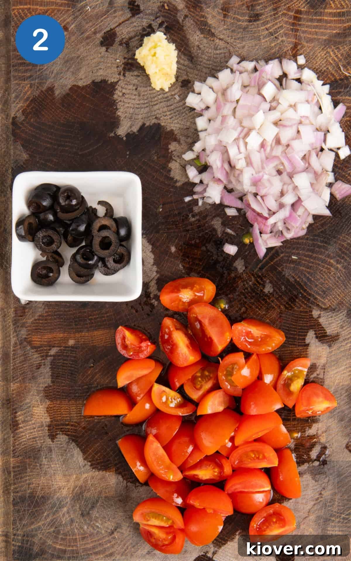 cherry tomatoes, olives, garlic and shallot on a cutting board.