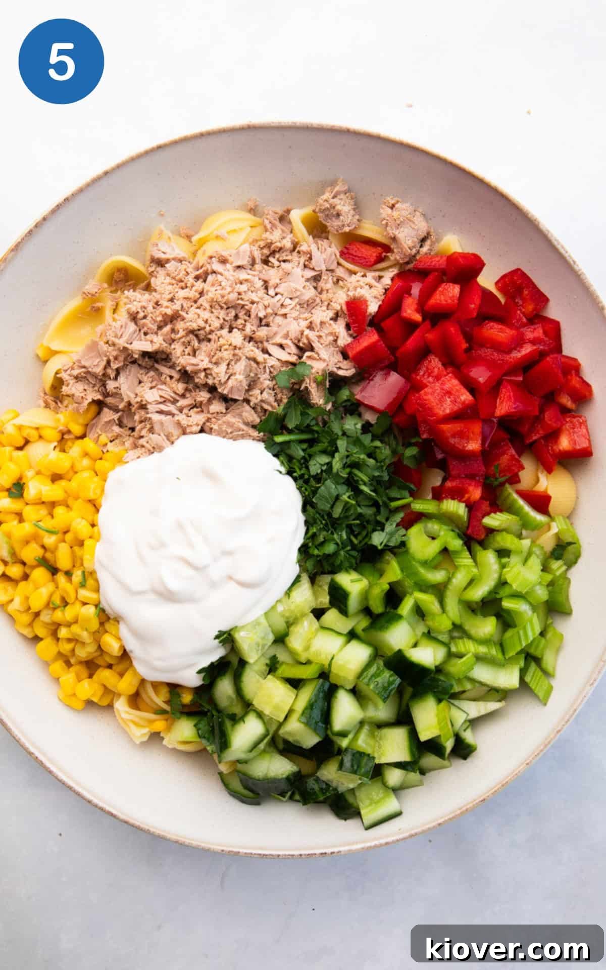Creamy Tuna Pasta Salad with Lemon and Fresh Herbs 8 Adding the chopped celery, pepper, cucumber, chopped parsley, tinned sweetcorn, tinned tuna and dressing to the bowl.