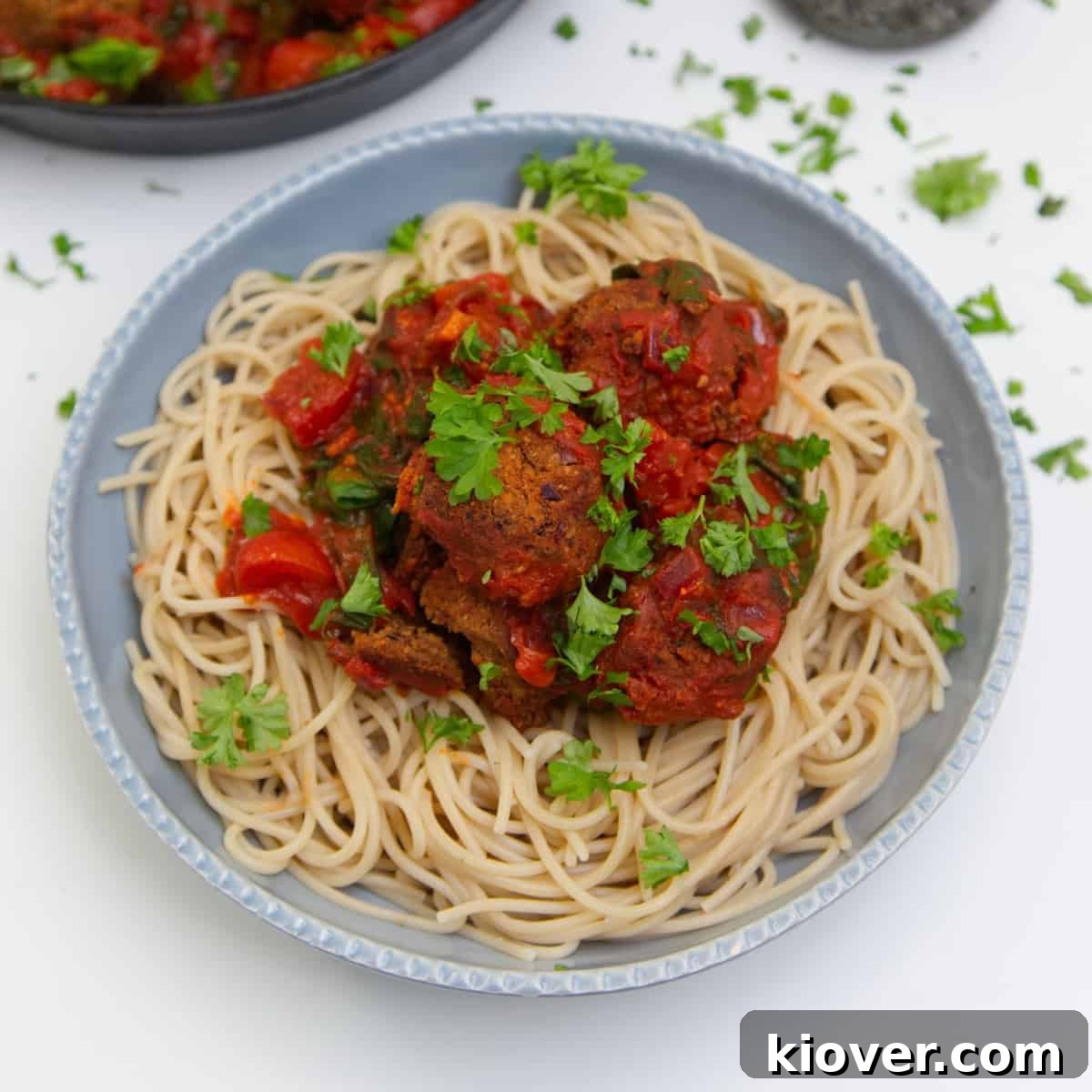 Spaghetti meatballs in a blue/grey bowl on white surface.