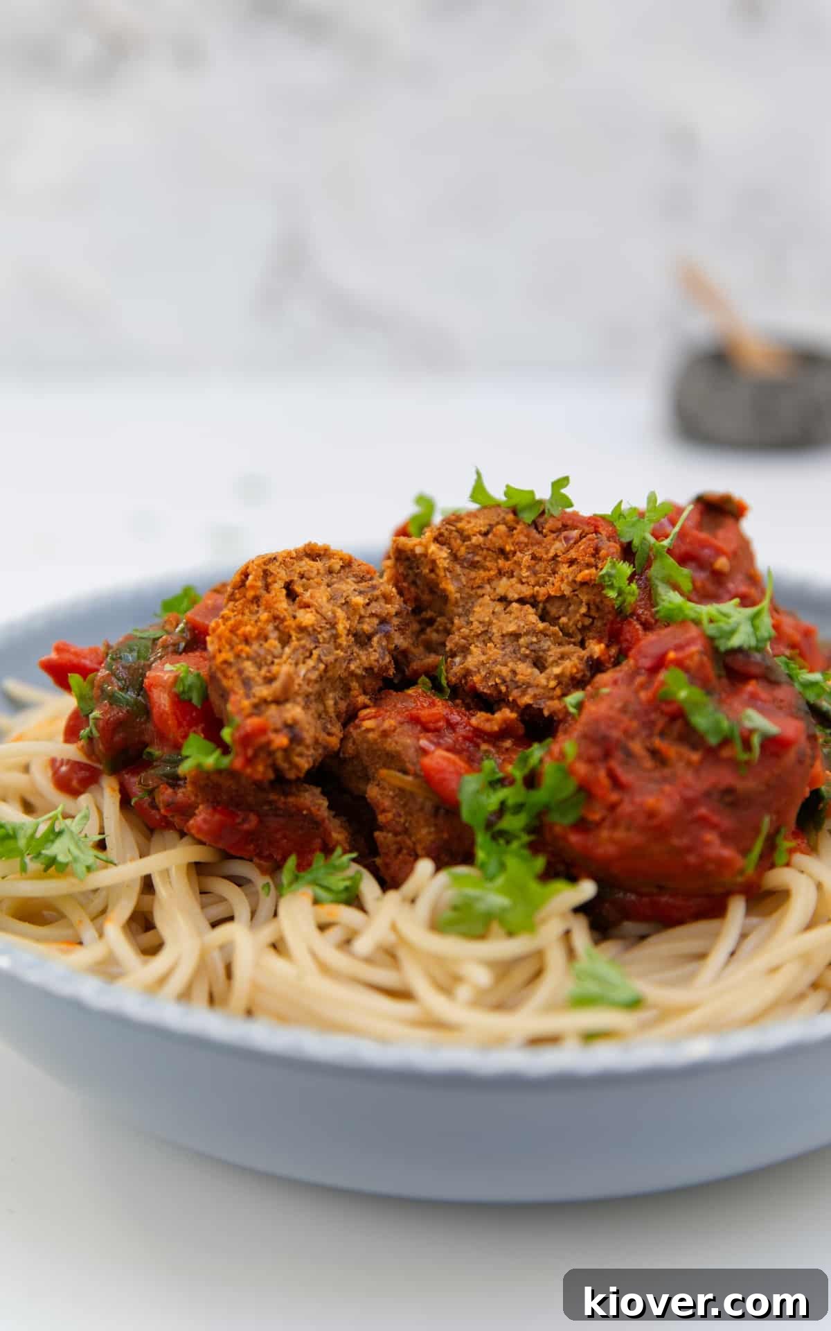 vegan meat balls cut open on a bed of spaghetti on blue/grey bowl.