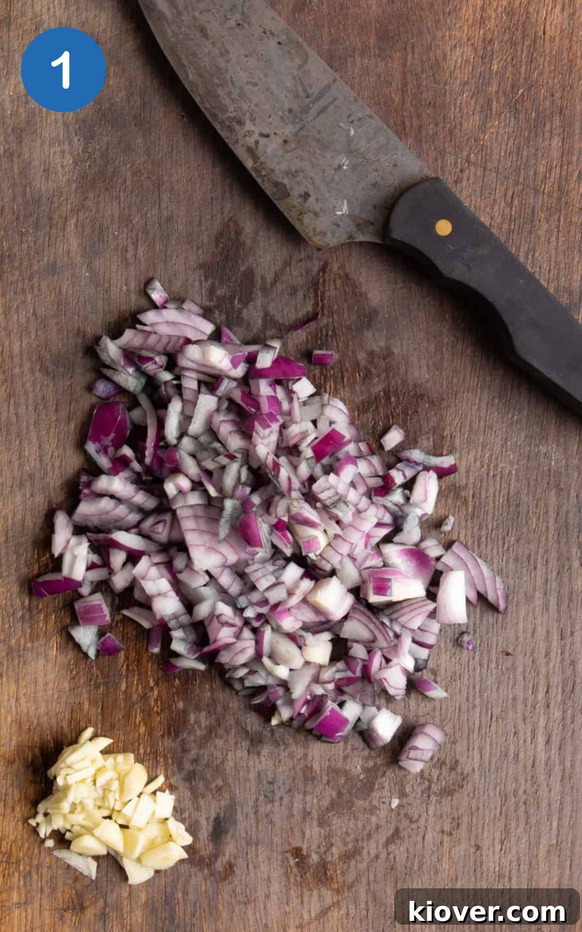 chopped onion and garlic on dark wooden chopping board with sharp knife.