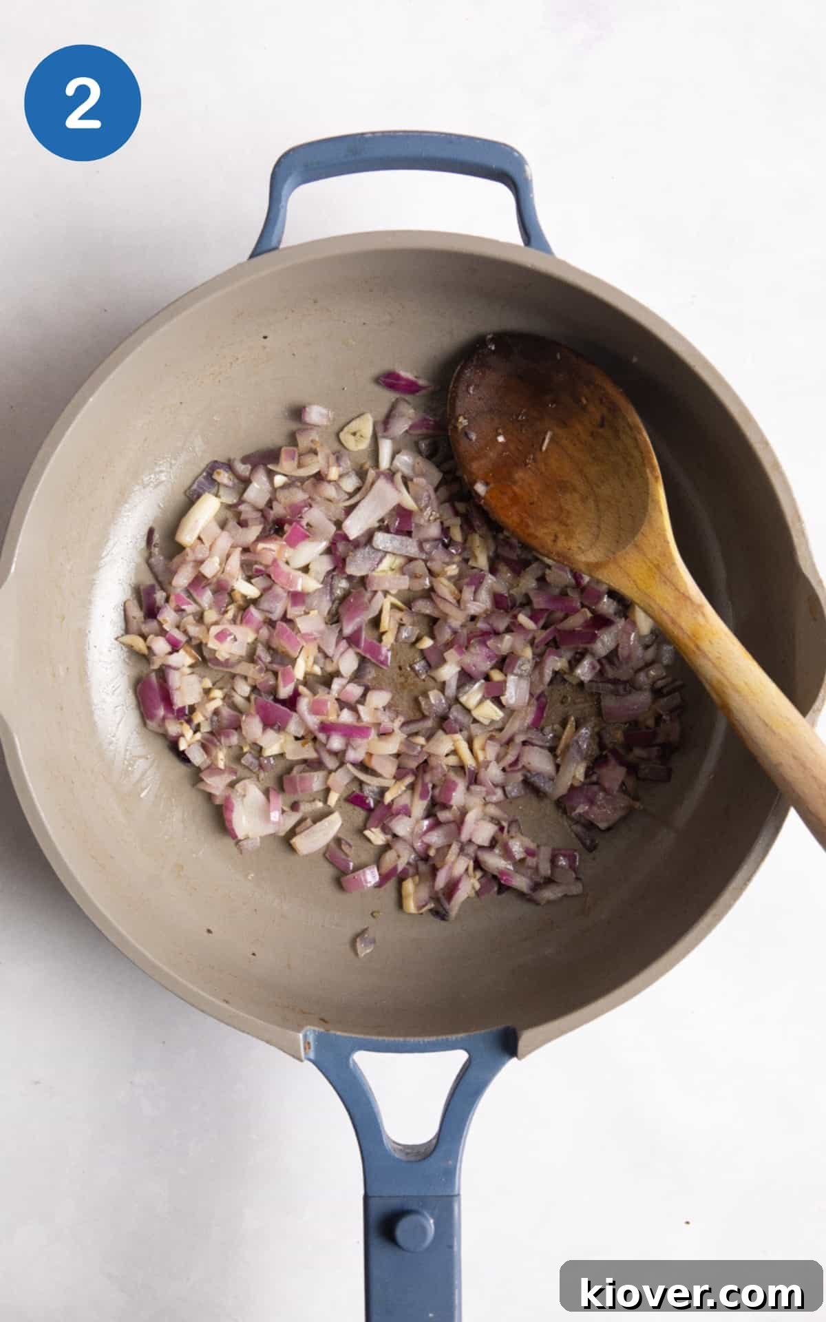 onions and garlic being fried in large blue non-stick frying pan.