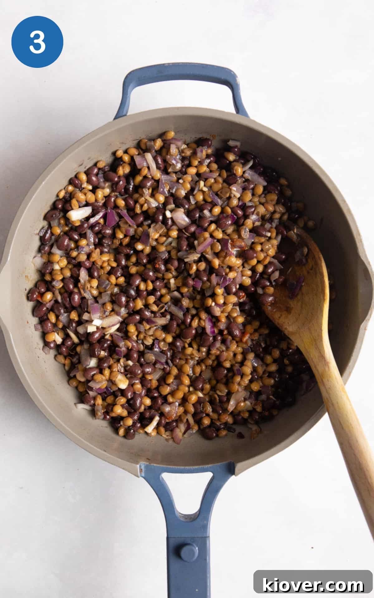 Lentils, black beans being fried with onions and garlic in large pan.