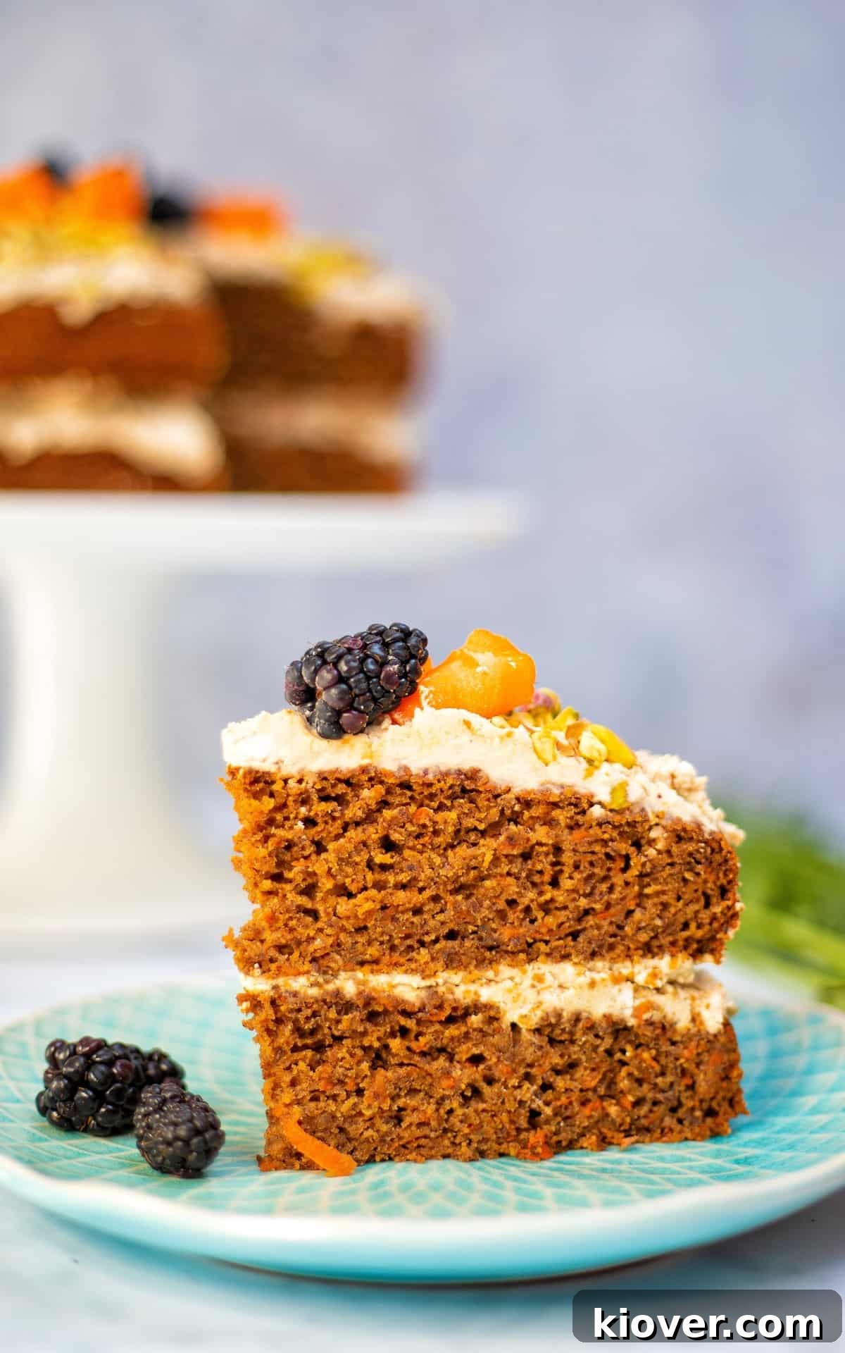 slice of carrot cake topped with blackberries on blue plate.