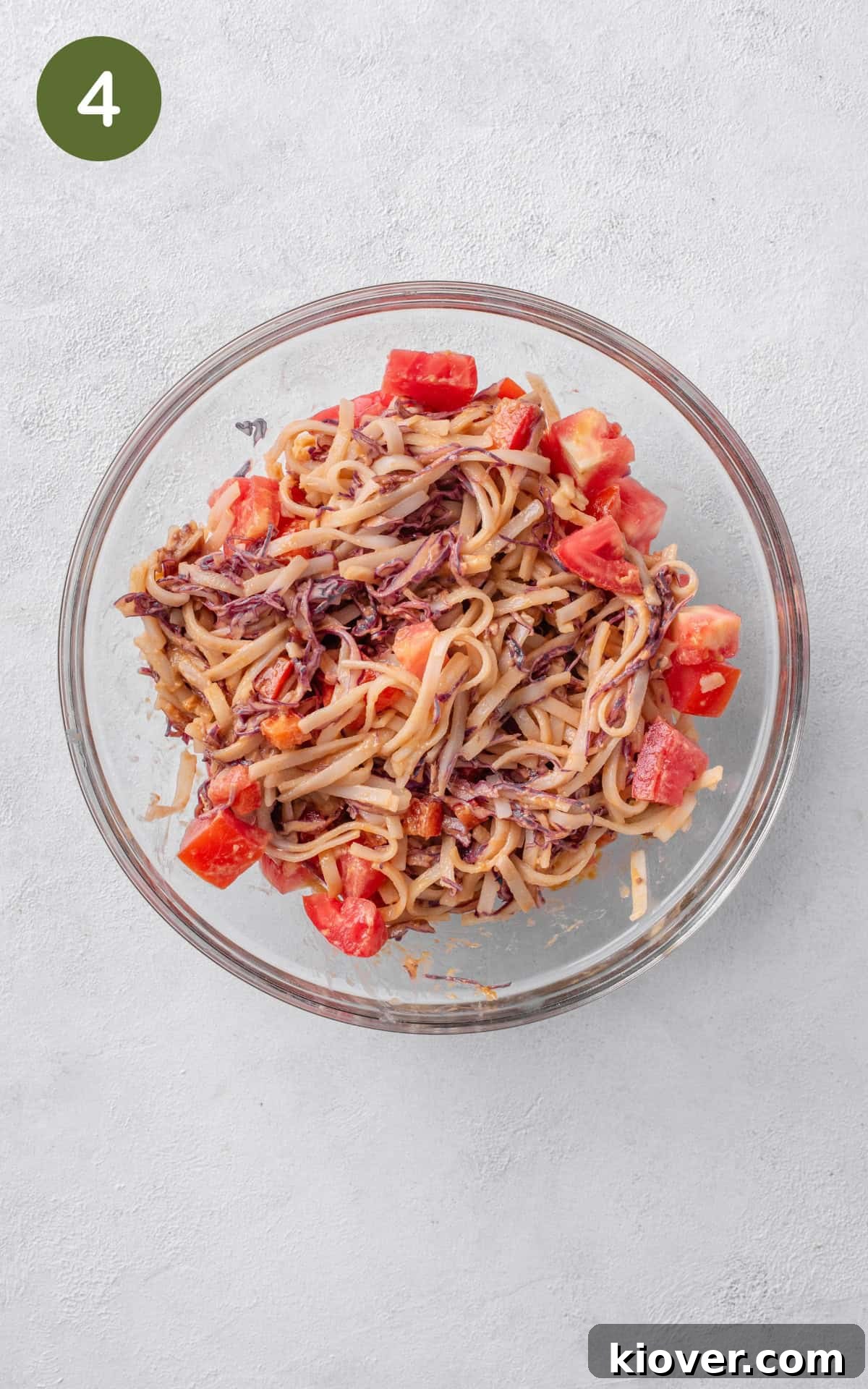 mixing the noodles with vegetables and dressing.