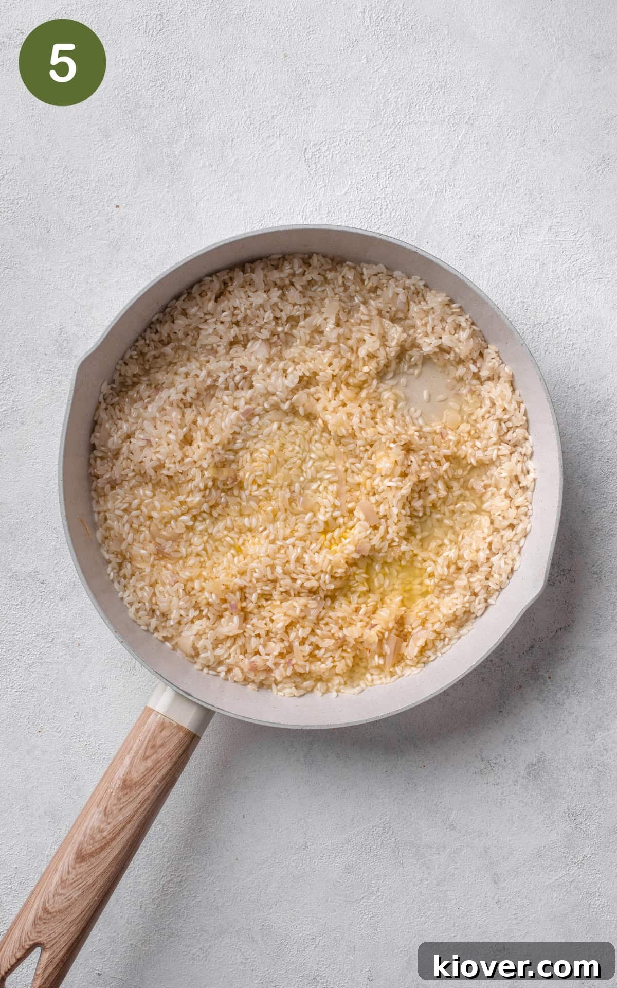 rice mixed with chicken stock in a frying pan.