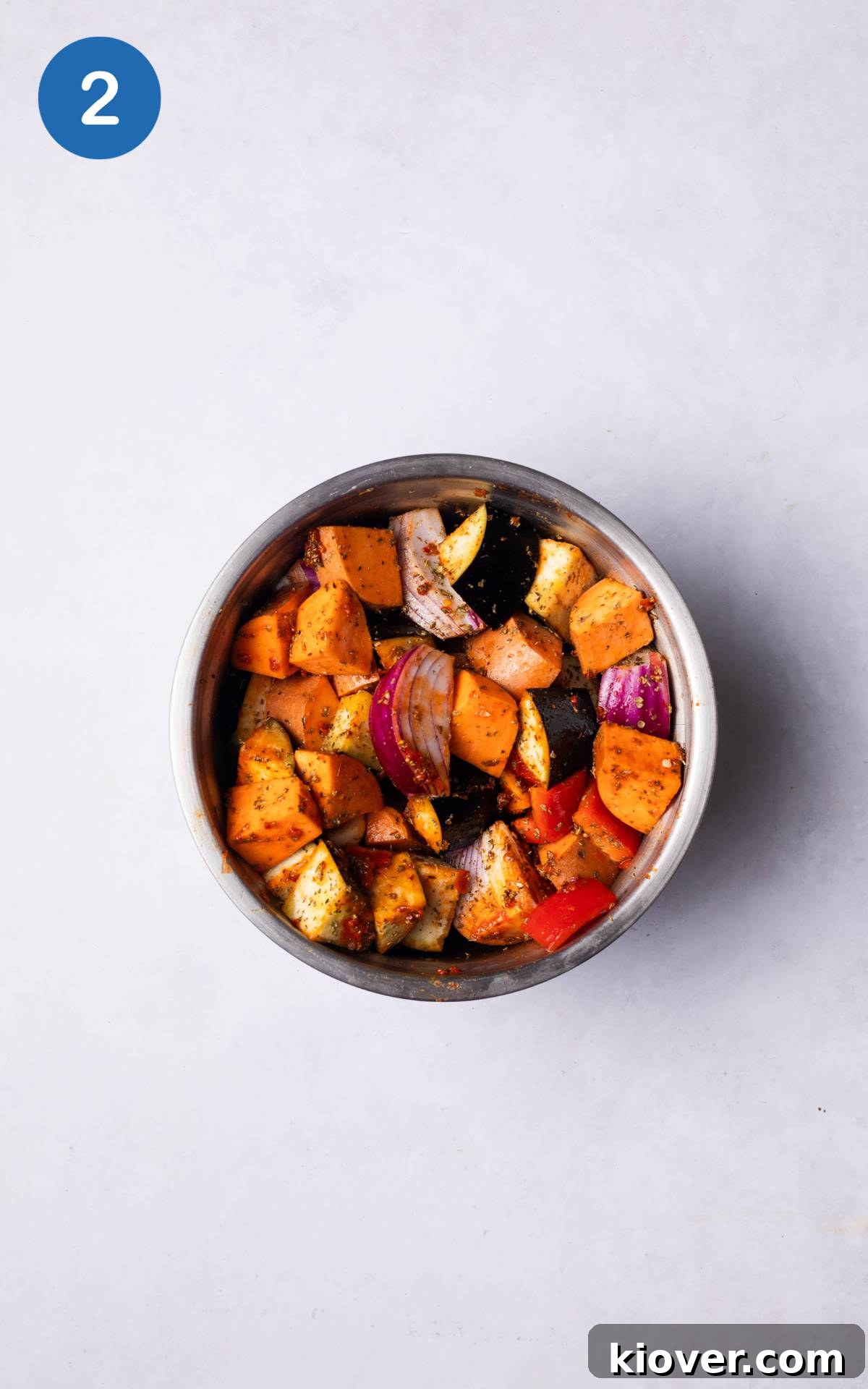 Sausage Tray Bake Recipe with Roasted Veggies and Herb Gravy 5 covering the vegetables with harrisa paste and spices in a bowl.