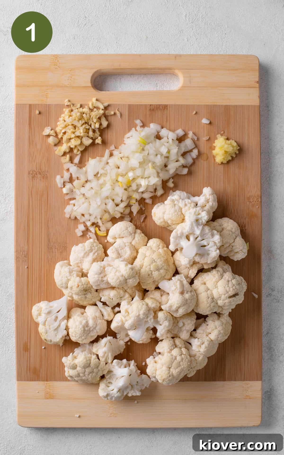 chopped cauliflower with onion and garlic on a wooden chopping board.