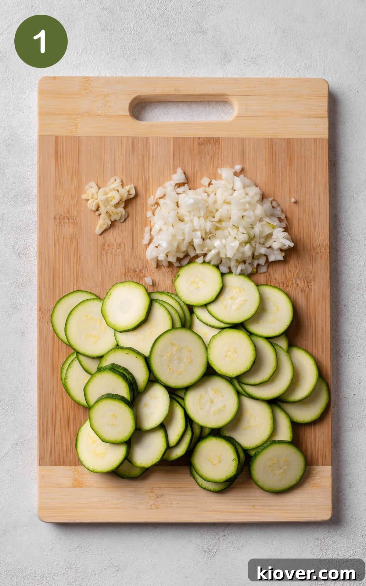Courgette, chopped garlic and chopped onion on a chopping board.