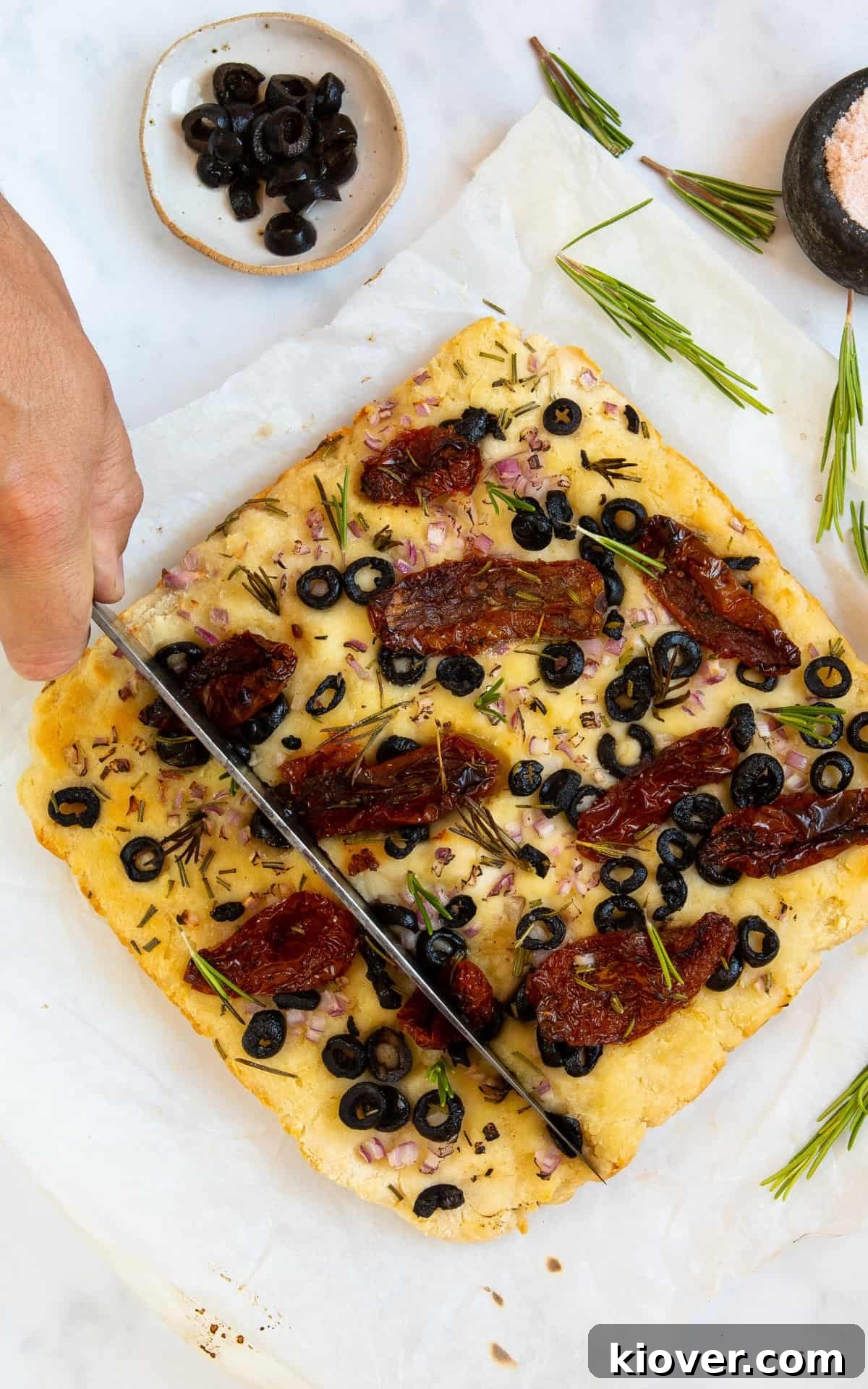 focaccia topped by sun dried tomatoes being cut by knife 