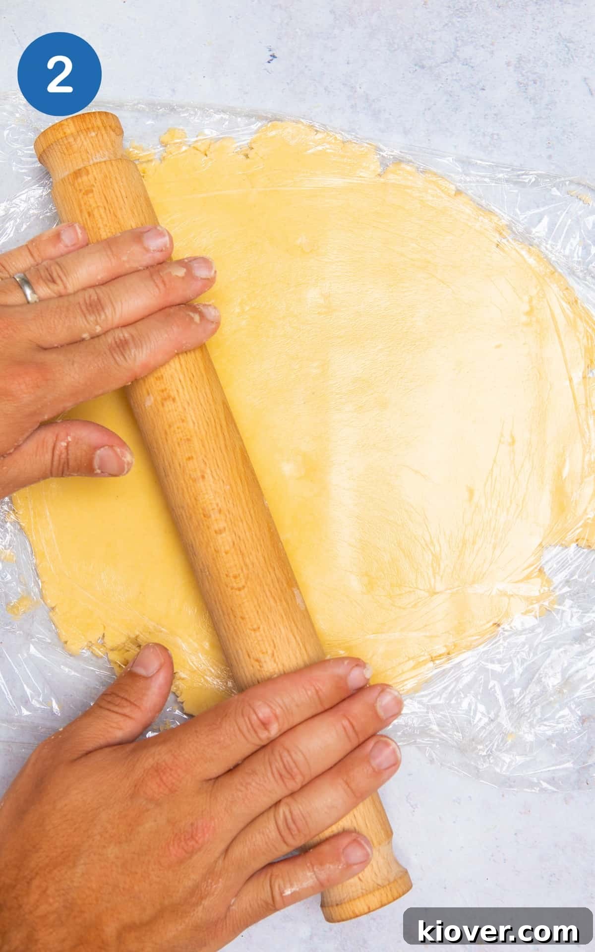 pastry being rolled out with rolling pin on grey marble surface.