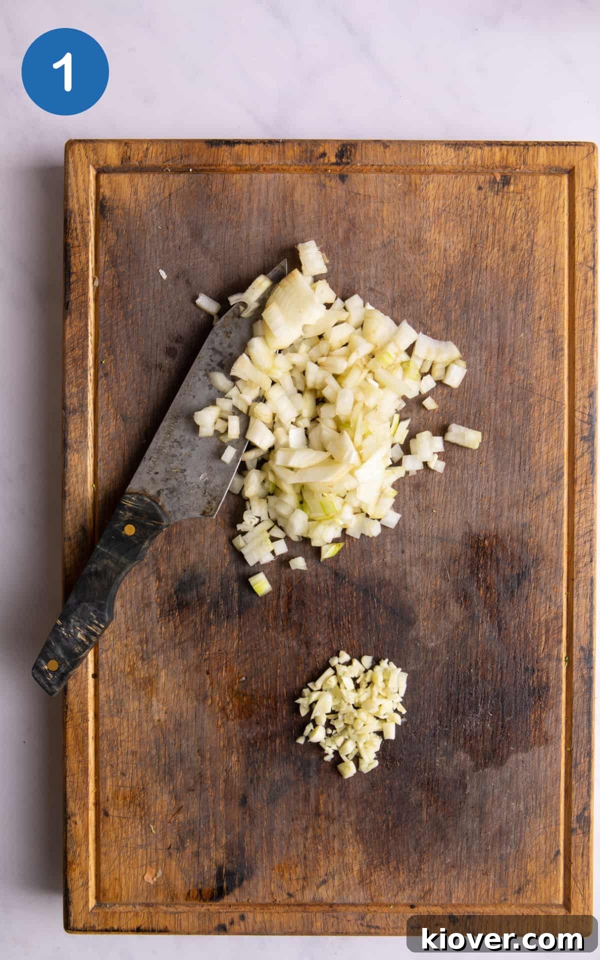finely chopped onion and garlic on dark wood chopping board with knife.