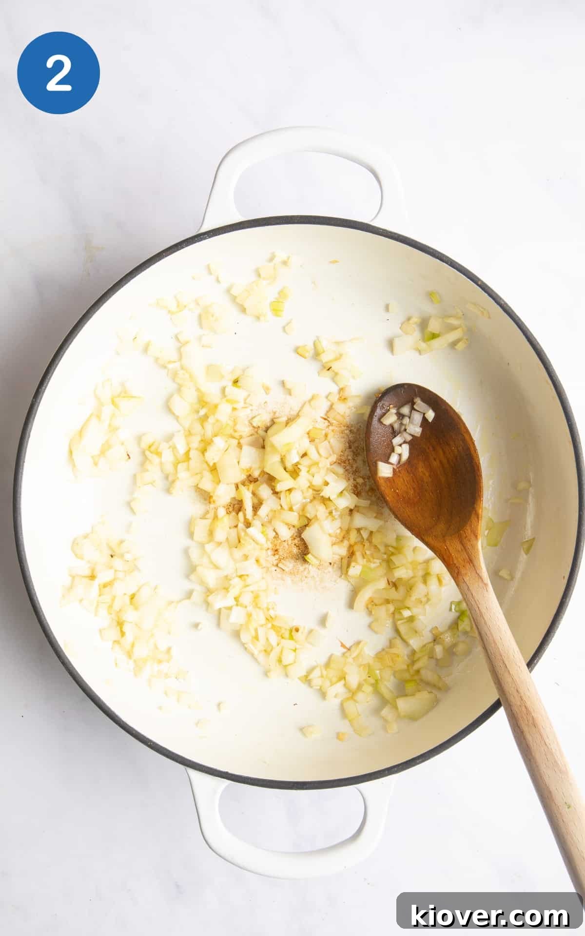 fried onions in large white casserole dish with wooden spoon. Dish is on white marble background.
