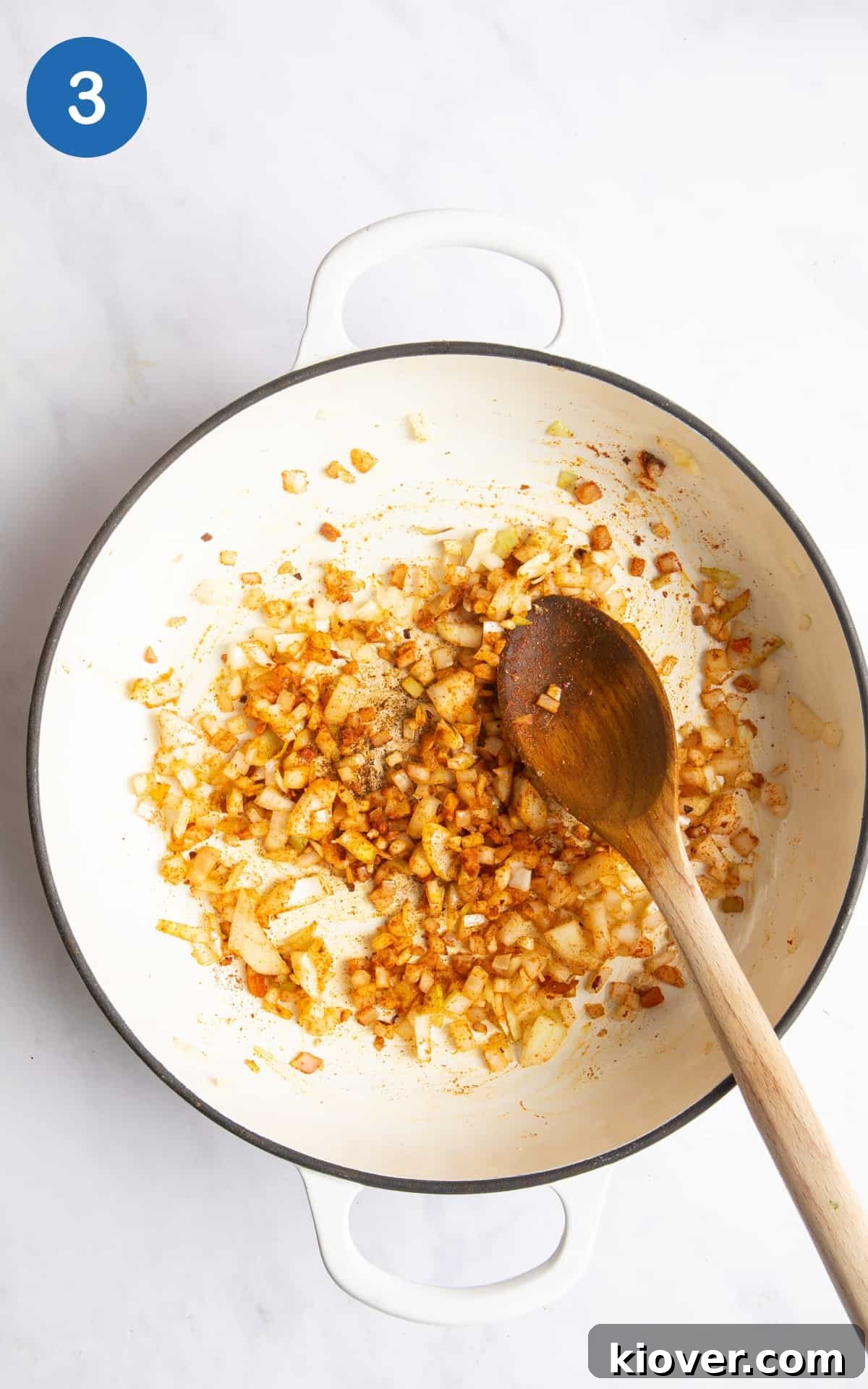 fried onions and spices in large white casserole dish with wooden spoon. Dish is on white marble background.