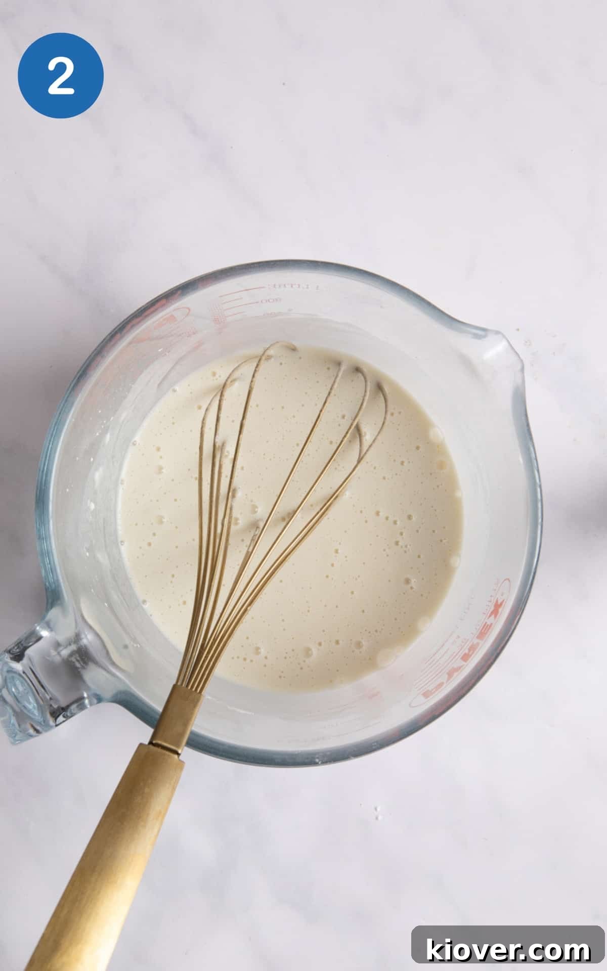 Gluten-Free Vegan Yorkshire Puddings Recipe 5 batter for Yorkshire puddings in large measuring jug with whisk in it. Measuring jug is on white background.