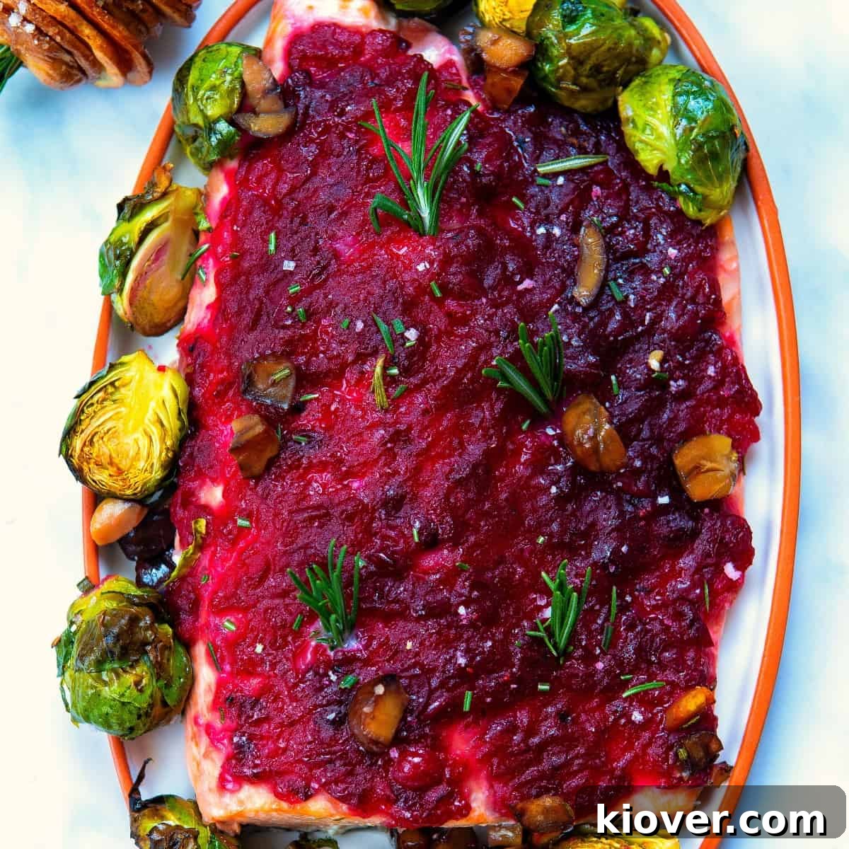 Festive Baked Salmon for Christmas Dinner 2 baked christmas salmon served with cranberry sauce an brussels sprouts on a white plate.