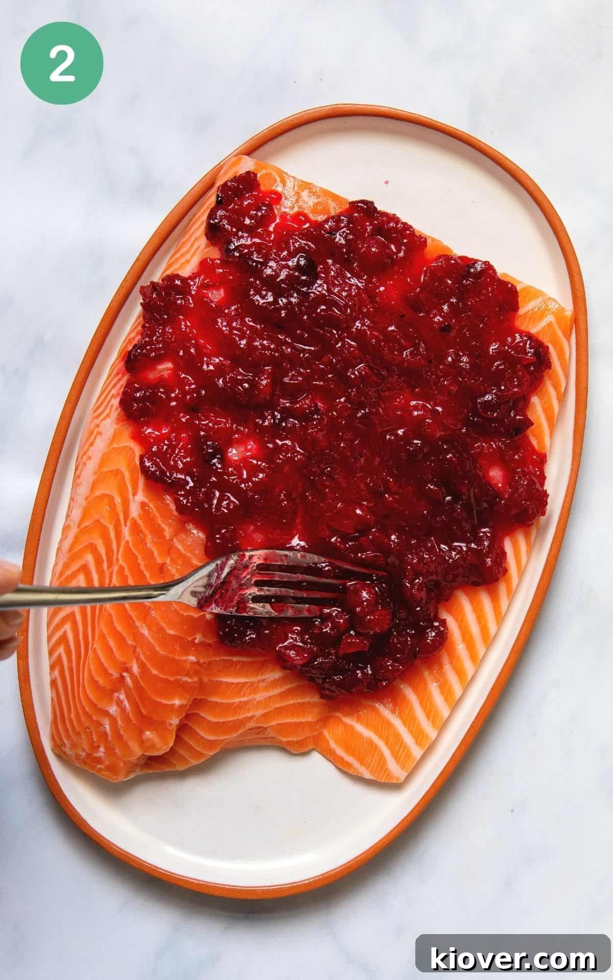 Festive Baked Salmon for Christmas Dinner 5 Spreading cranberry sauce with a fork onto a salmon fillet before baking.