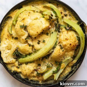 Cooked Cauliflower Cheese in black skillet pan. Pan is displayed on white marble background