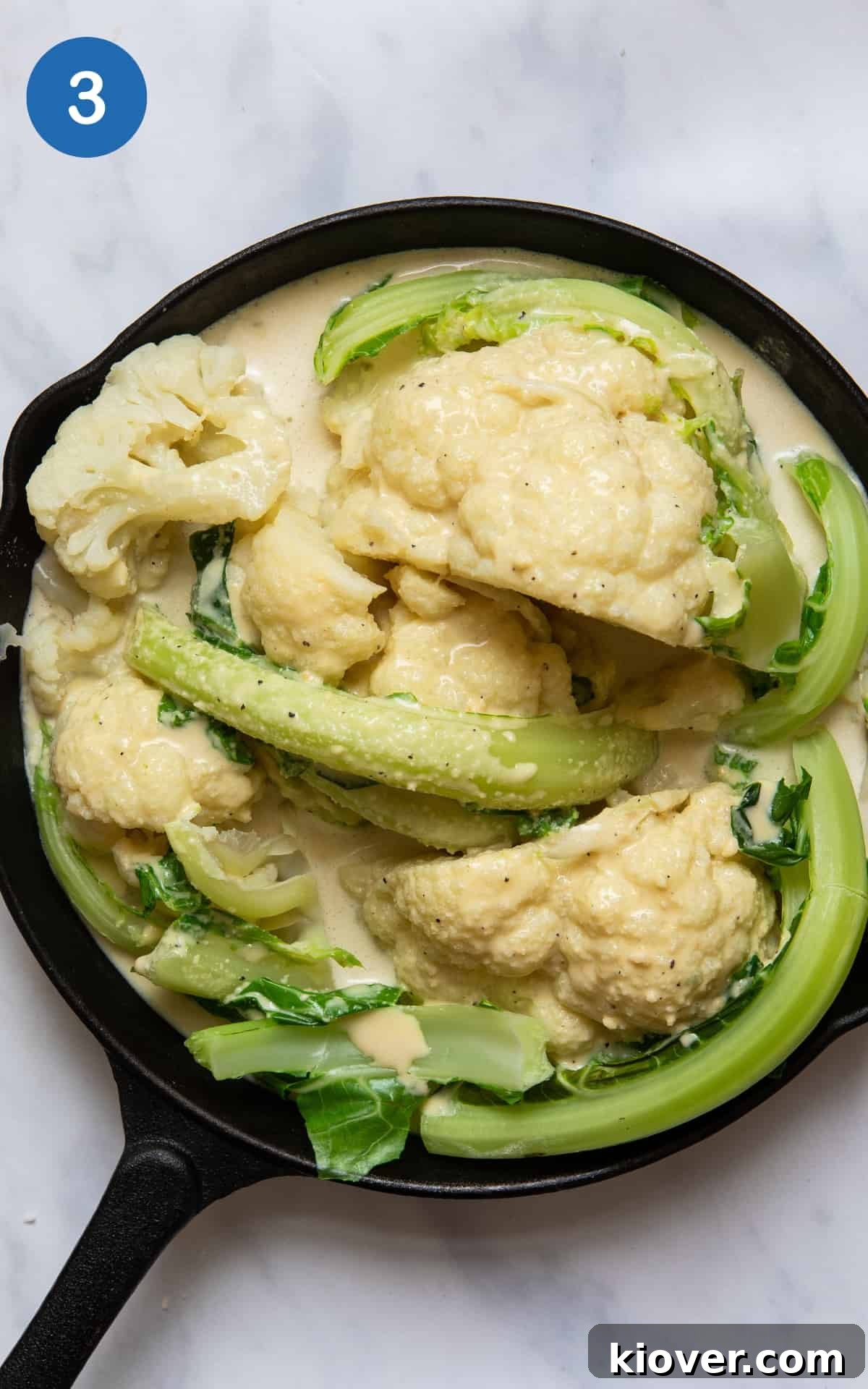 Pre-cooked cauliflower cheese in black skillet pan. Skillet pan is on white marble background. 