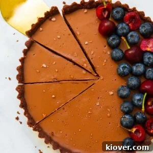 overhead of vegan chocolate tart sliced with golden cake slice and topped with berries.