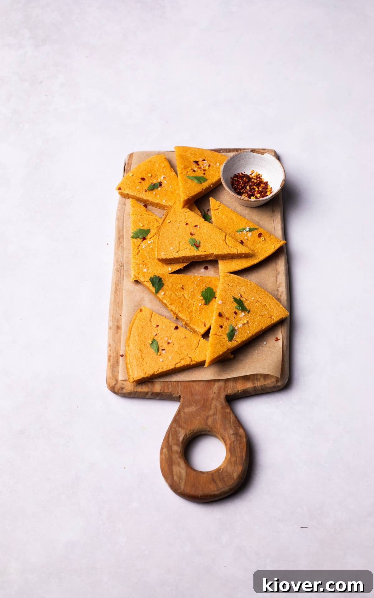 Crispy Socca Chickpea Pancake Recipe for Beginners 7 sliced Socca topped with chilli flakes and salt on a wooden board.