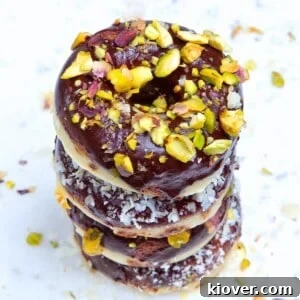4 doughnuts stacked on a white marble background with pistachio and coconut toppings.