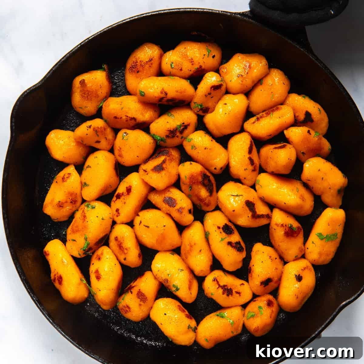 Sweet Potato Gnocchi Recipe: Light, Fluffy & Flavorful 2 Sweet Potato Gnocchi in black frying pan. Pan is displayed on white background.