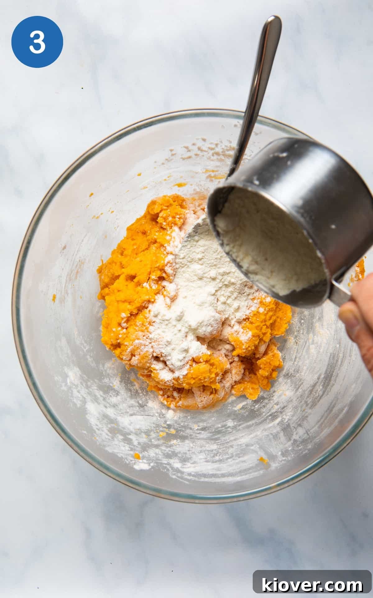 Sweet Potato Gnocchi Recipe: Light, Fluffy & Flavorful 6 Flour being added to large mixing bowl with sweet potato in it. Bowl is on white background.