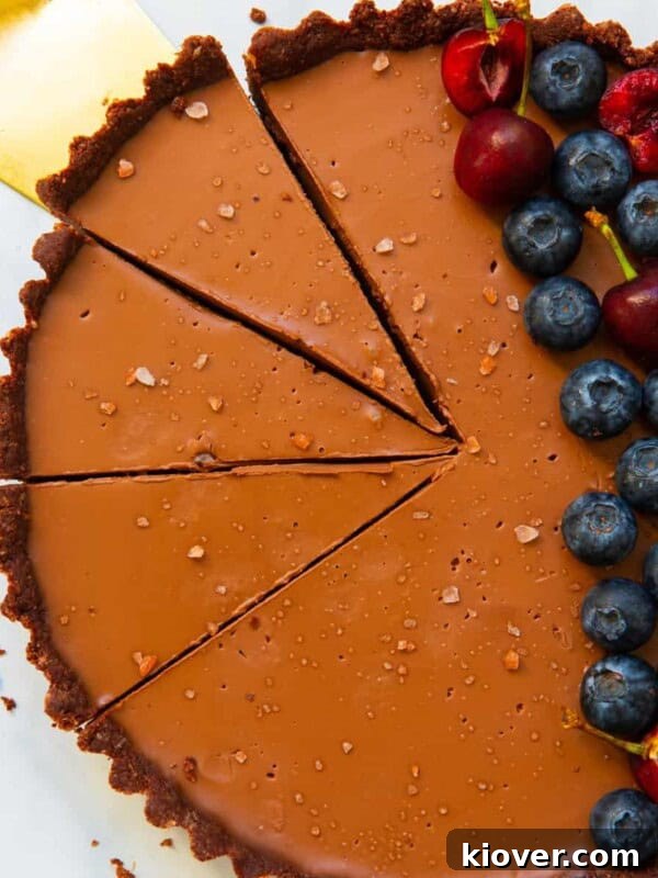 overhead of vegan chocolate tart sliced with golden cake slice and topped with berries.