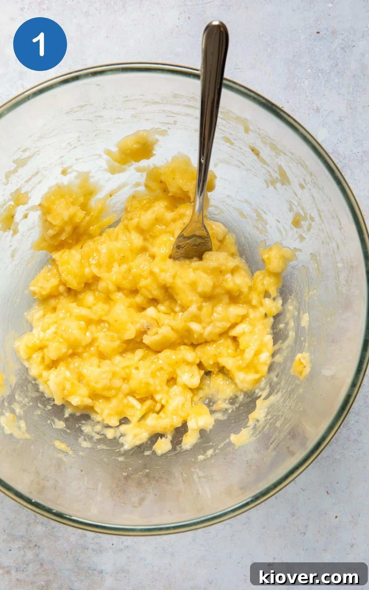 bananas being mashed in a large mixing bowl with a fork.