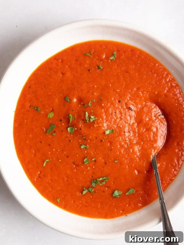 red pepper and tomato soup served in a white bowl with a spoon inside.