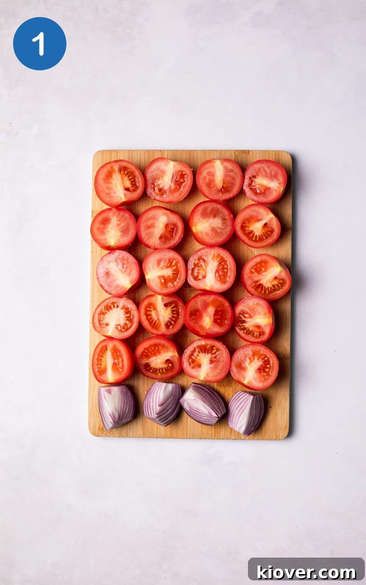 Tomatoes sliced in half and onions sliced in quarters lined up on a wooden chopping board.