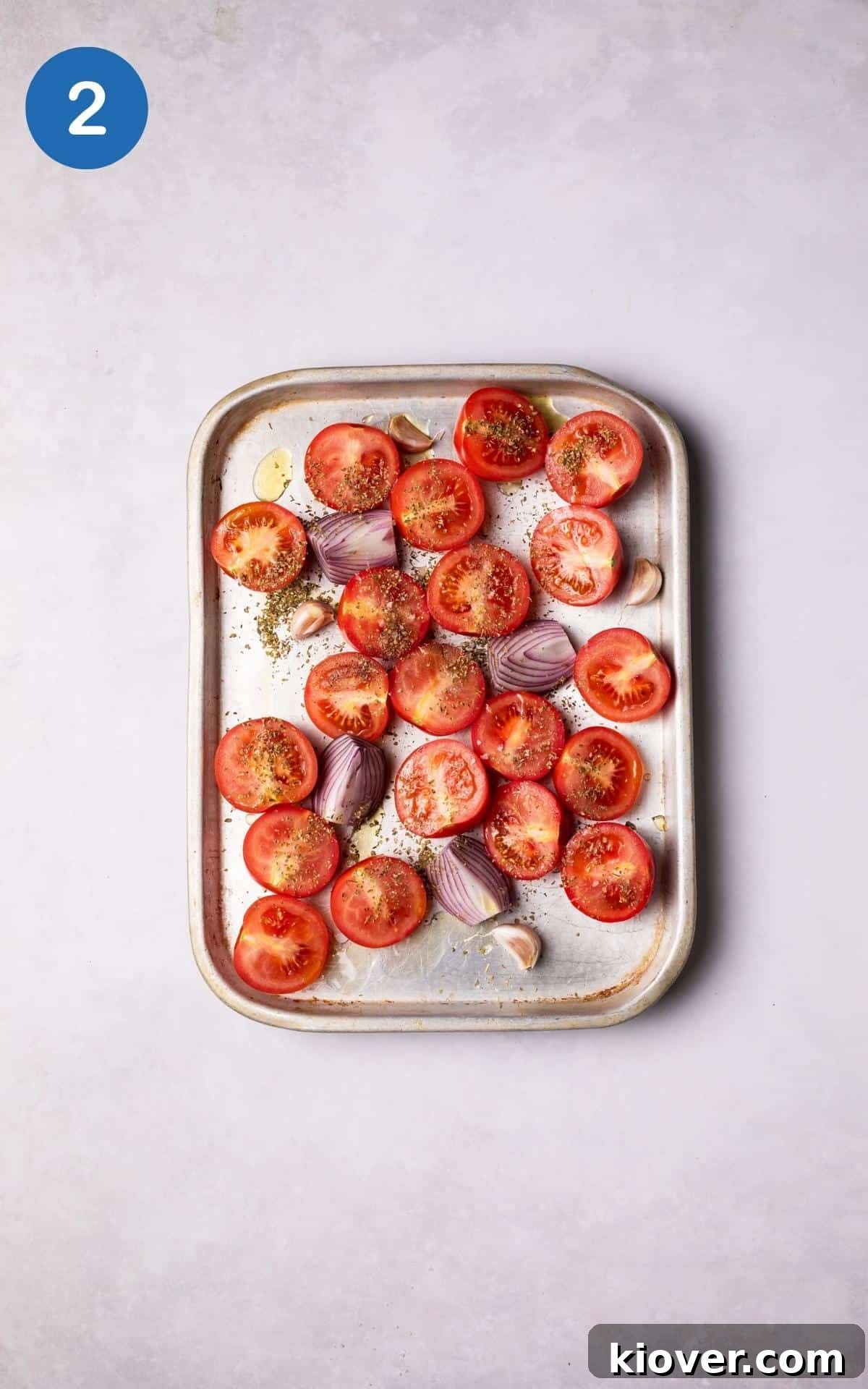 Tomatoes, onions and garlic cloves with spices on a baking tray.