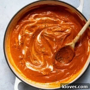 Tomato soup in a large pot with a wooden spoon. Pot is displayed on a white marble background.