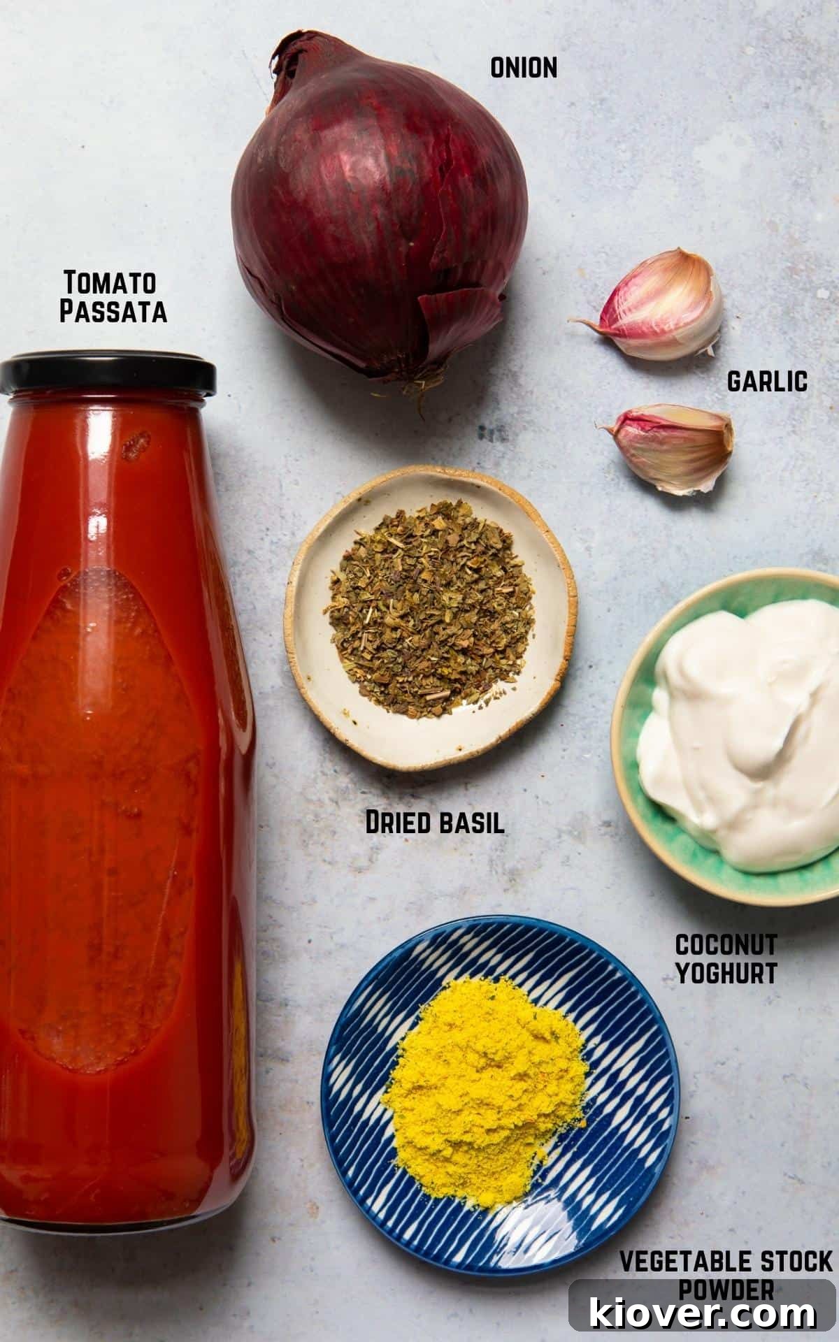 ingredients to make tomato soup laid out on a white marble background.