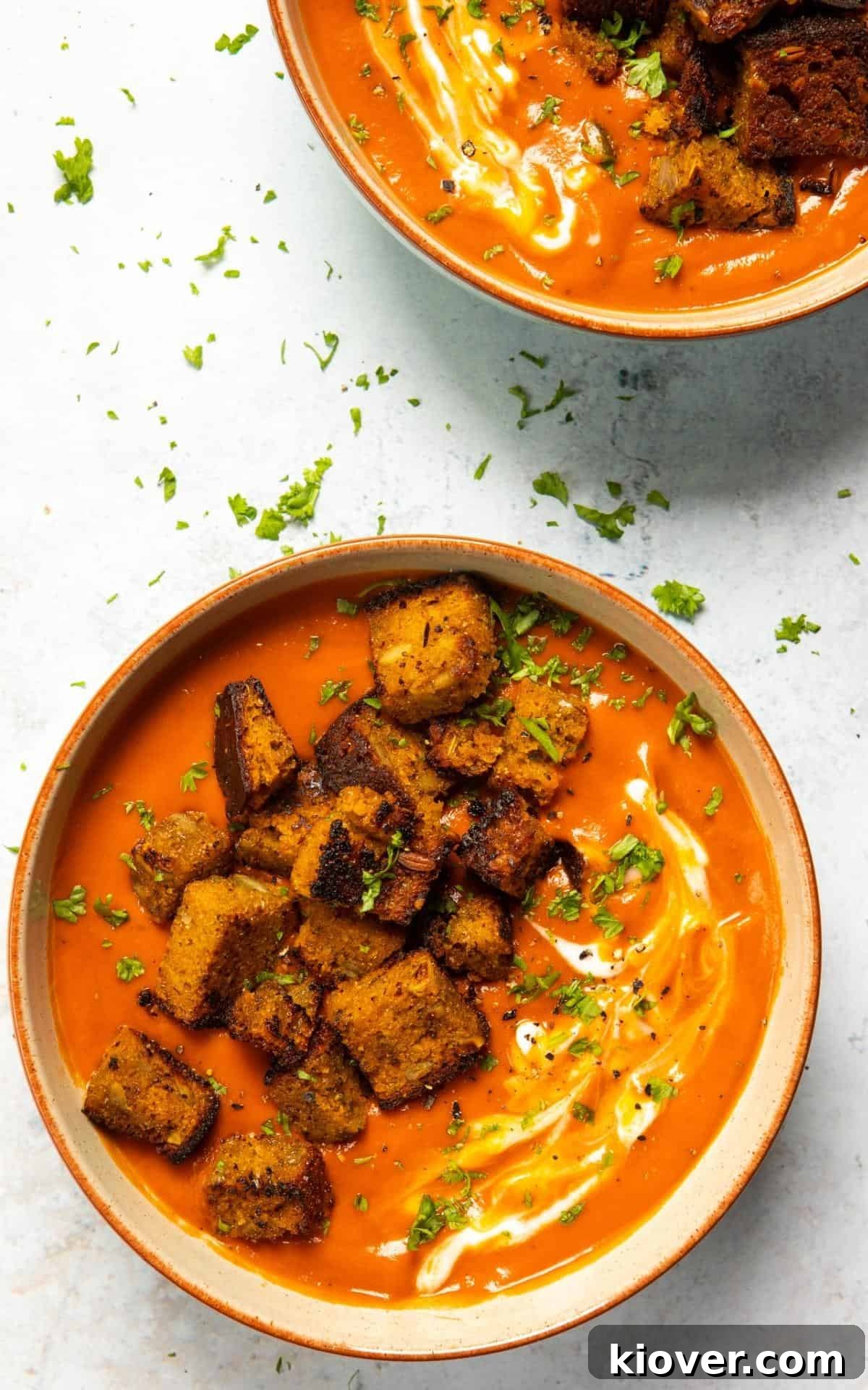 Bowl of tomato soup with croutons and chopped basil on top.