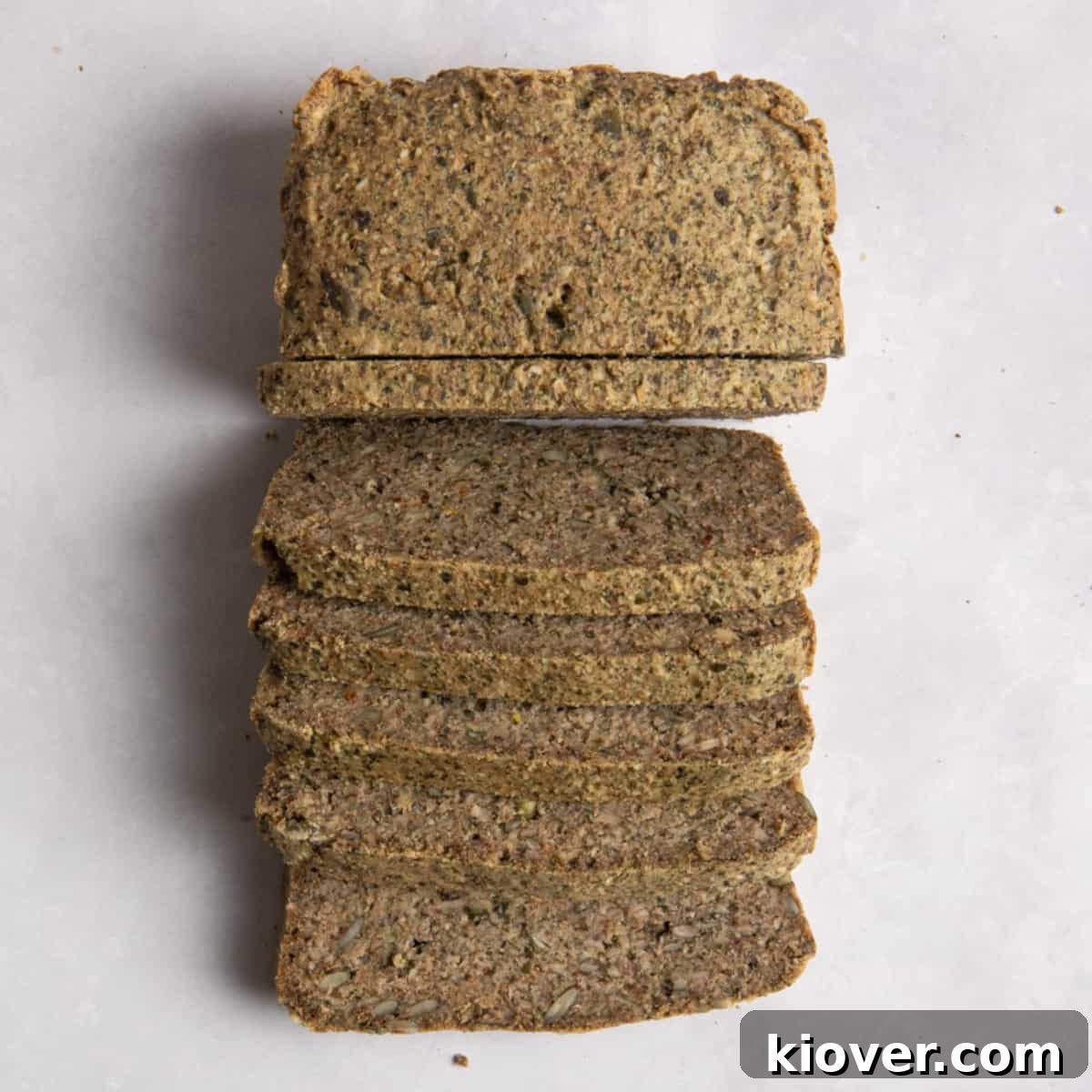 Overhead shot of sliced seeded bread on white surface.