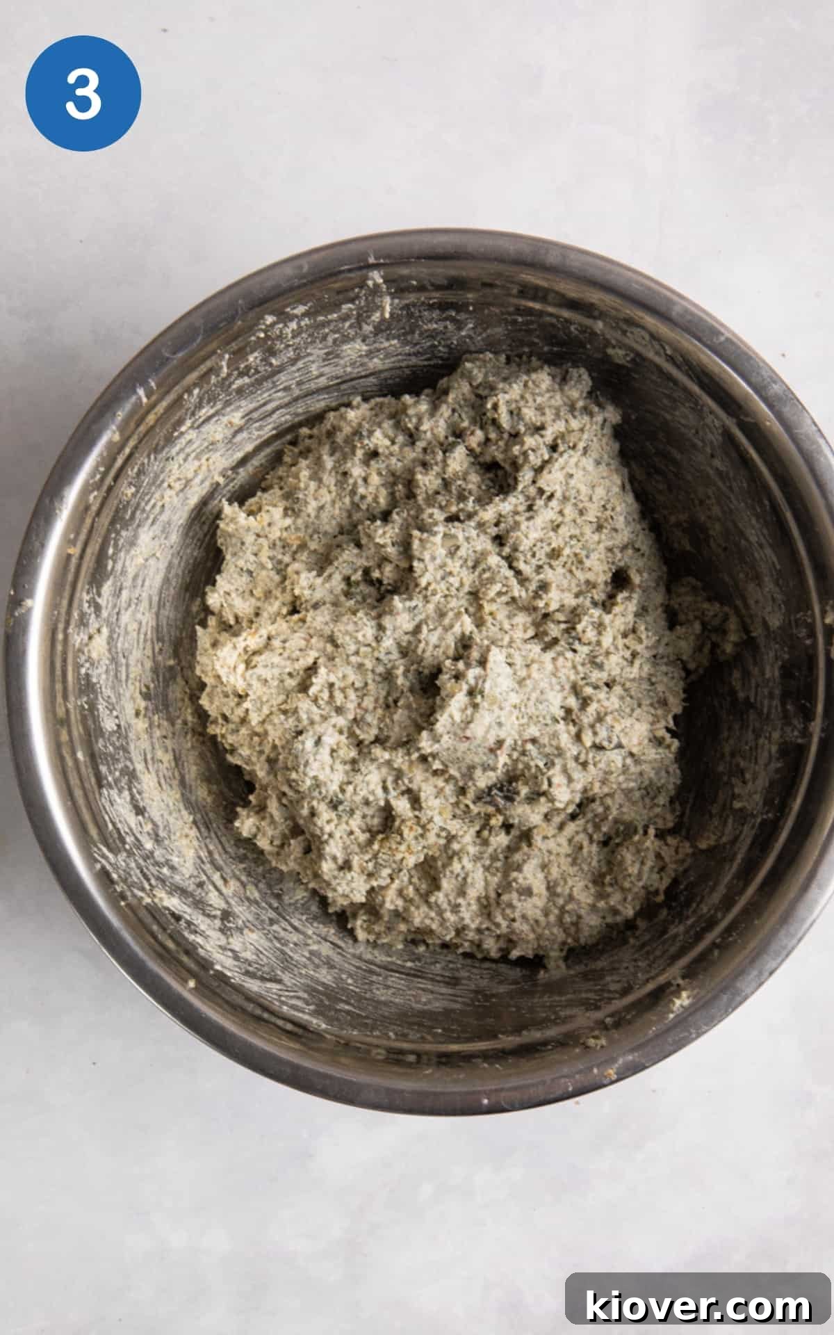 bread dough in silver mixing bowl on white surface.