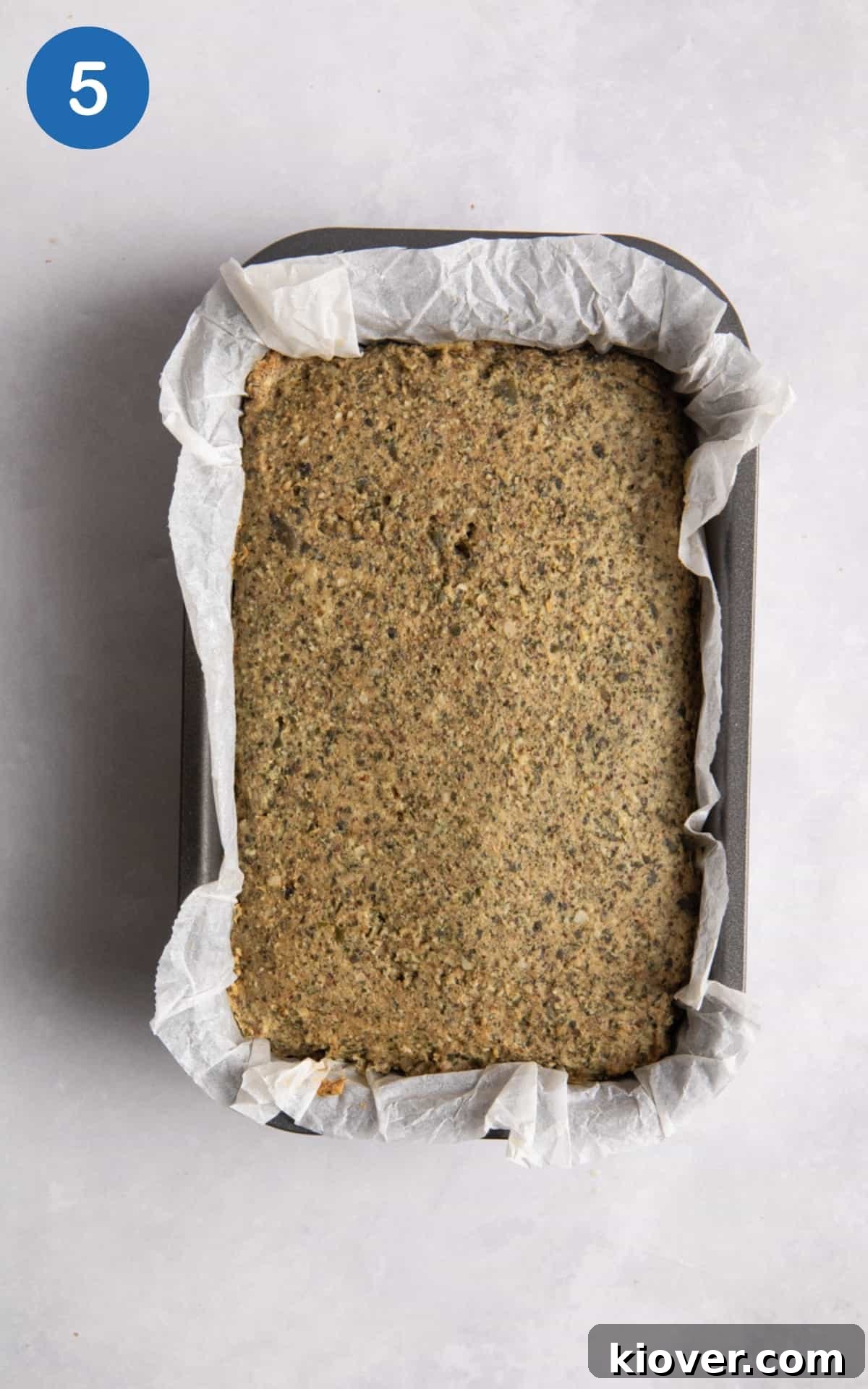 Gluten Free seeded loaf in break loaf tin with parchment paper on white surface.