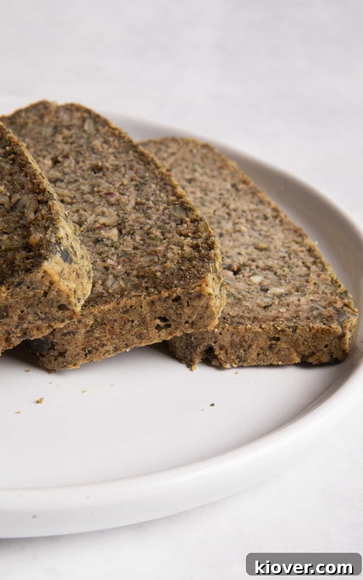 sliced seeded bread on white plate on white surface.