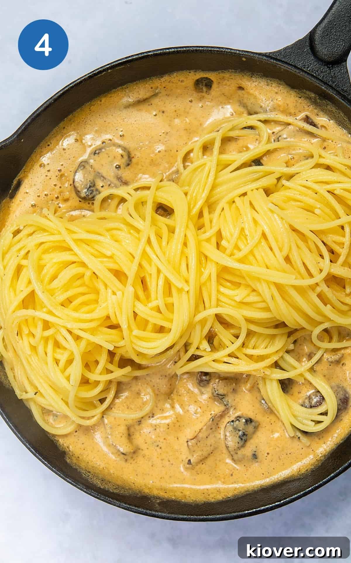 Creamy Mushroom Alfredo Pasta Recipe for Dinner 7 Adding pasta to the sauce with mushrooms in a pan.